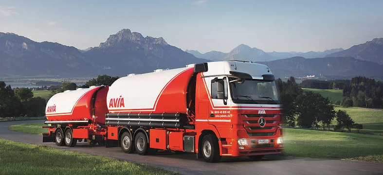 Pojazd dostawczy z logo AVÍA zaparkowany przed zbiornikiem magazynowym. Ciężarówka naczepowa z oznaczeniem AVIA oraz cechami Mercedes-Benz. Idealna do transportu towarowego.