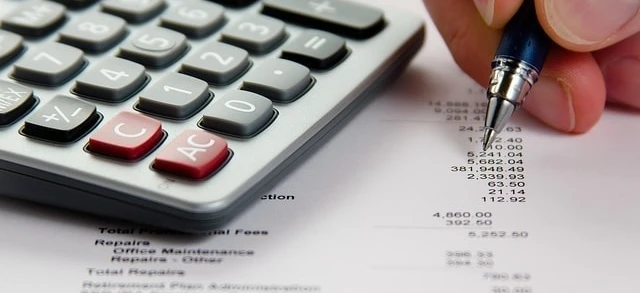 Biurko biurowe z kalkulatorem, papierem i innymi artykułami biurowymi do obliczania całkowitych kosztów i wydatków. Słowa kluczowe obejmują sprzęt biurowy, artykuły papiernicze, dokumenty i przybory do pisania. Podsumowanie liczb na potrzeby utrzymania biura oraz napraw.