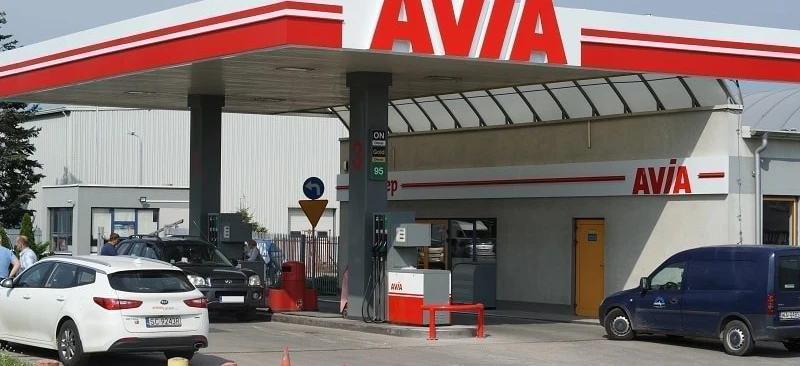 Samochód rodziny zaparkowany na stacji benzynowej z widoczną tablicą rejestracyjną pojazdu "5C92438". Samochód ma złoty zderzak, lusterko samochodowe i boczne lusterko.