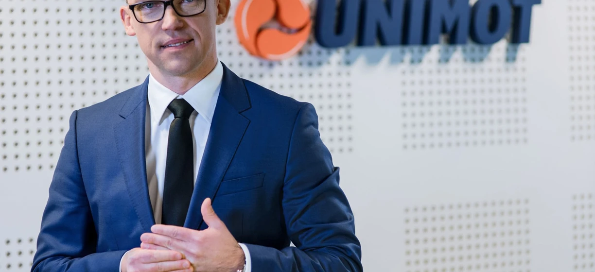 Pracownik umysłowy w formalnym stroju składającym się z marynarki i koszuli z logo UNIMOT. Profesjonalny strój do pracy w branży technologicznej.