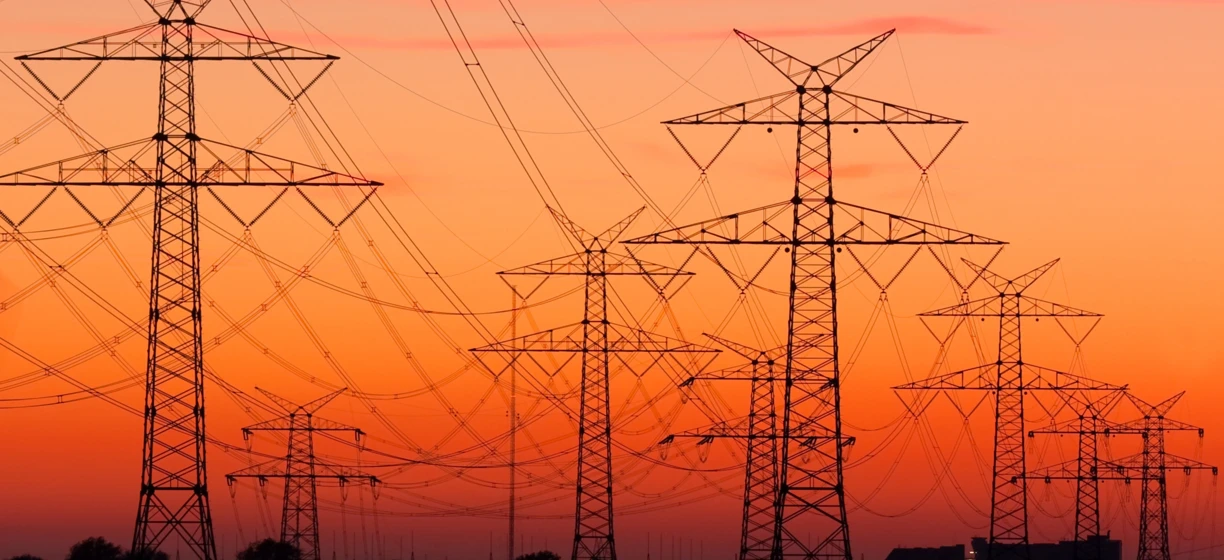 Linia przesyłowa i wieża przesyłowa o zmierzchu, dostarczająca elektryczność do pomarańczowego blasku miasta. Istotna część sieci elektroenergetycznej.