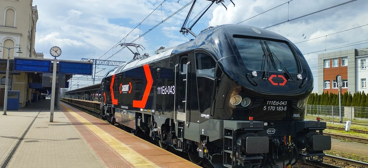 Nowoczesna lokomotywa zasilana elektrycznie podróżuje po torach pod napiętymi liniami zasilającymi w Polsce. Transport publiczny jest niezbędny dla efektywnego przemieszczania ludzi i towarów.