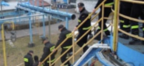 Grupa robotników noszących odzież roboczą o wysokiej widoczności i kaski stoi przy płocie. Załoga jest gotowa na dzień pracy.