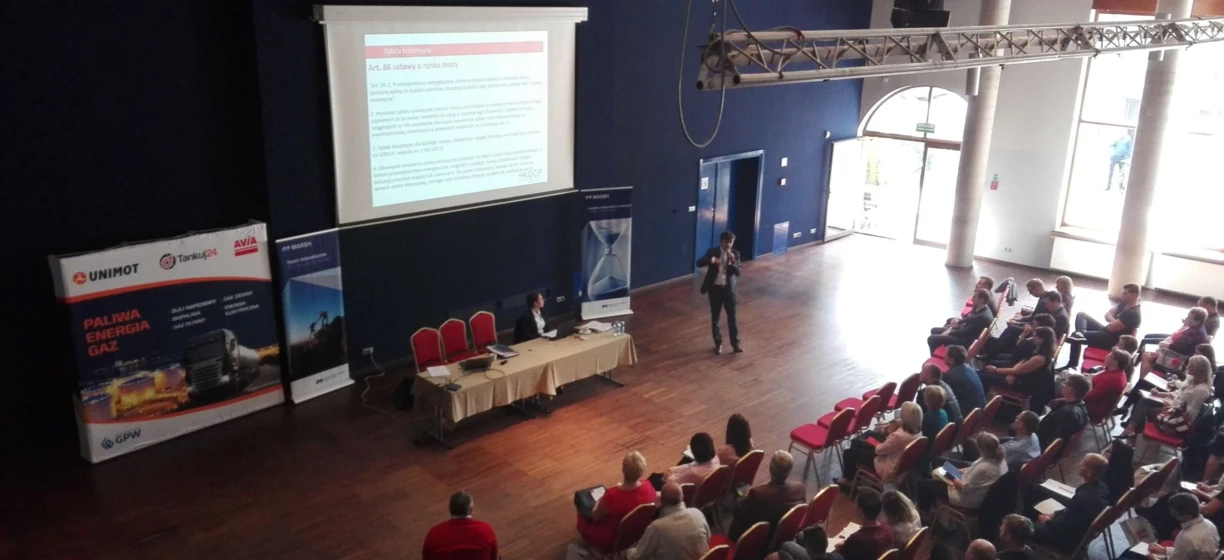 Publiczność na wydarzeniu technologicznym w sali konferencyjnej sponsorowanej przez UNIMOT. Meble, krzesła i urządzenia do wyświetlania elektronicznego są przygotowane na to wydarzenie.