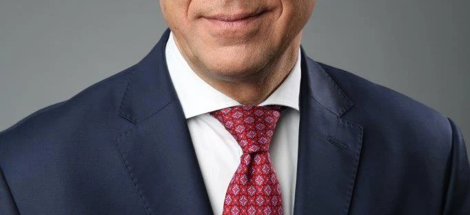 Osoba nosząca okulary, z podbródkiem oprzytym o dłoń, wyróżniająca pielęgnację wzroku i modę okularową. Szczegóły na ramionach, kołnierzu i rękawach są widoczne.