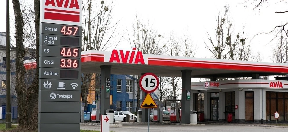 Pojazd zaparkowany na stacji benzynowej z różnymi opcjami paliwa, w tym olejem napędowym, Gold 95 i CNG. Wyraźnie widoczna marka AViA.