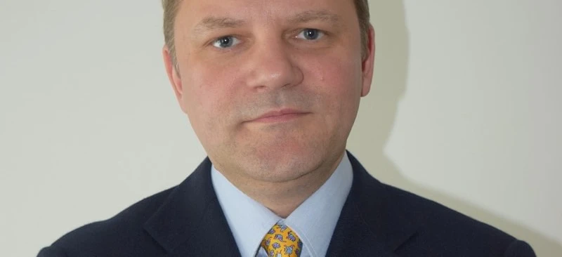 Zbliżenie obrazka mężczyzny w czarnym żakiecie i krawacie, pokazującego jego podbródek, brew, czoło i kołnierzyk, gdy pewnie pozuje.