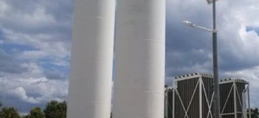 W przemyśle inżynier sprawdza cylindryczny materiał kompozytowy. W tle widoczne maszyny i rury.