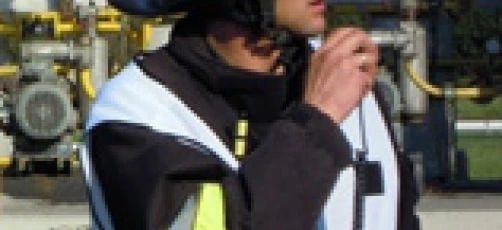 Robotnik fizyczny noszący osobistą odzież ochronną, w tym kask i odzież odblaskową. Na obrazku widzimy pracownika służb ratowniczych, być może strażaka, w swoim ubraniu roboczym.