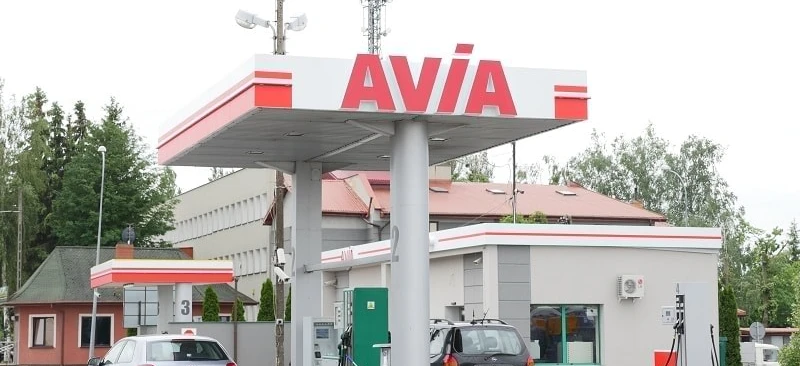 Samochód rodzinny zaparkowany przy stacji paliw z dystrybutorem paliwa w tle. Bumper, lusterka i tablica rejestracyjna pojazdu są widoczne. Loga AVIA i SD Eibar również są obecne.