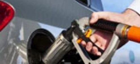 Dystrybutor paliwa na stacji benzynowej obok samochodu z otwartymi drzwiami i czyszczonym przednim szybą. Opieka nad pojazdem z napędem elektrycznym i maska w tle.