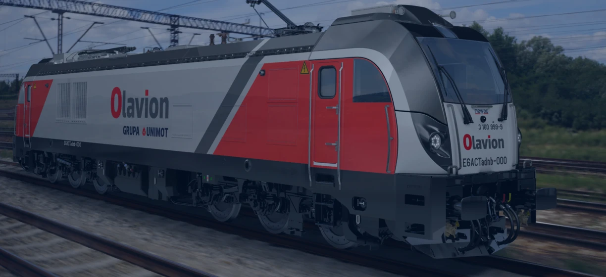 Elektryczna lokomotywa poruszająca się po torze, z wycieraczkami na przedniej szybie i włączonym reflektorem. Skupienie na ESACTadb-000.