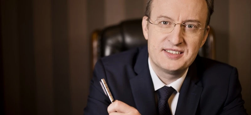 Zbliżenie osoby noszącej okulary i garnitur z palcem spoczywającym na brodzie. Opieka nad wzrokiem i formalne ubranie są tutaj podkreślone.