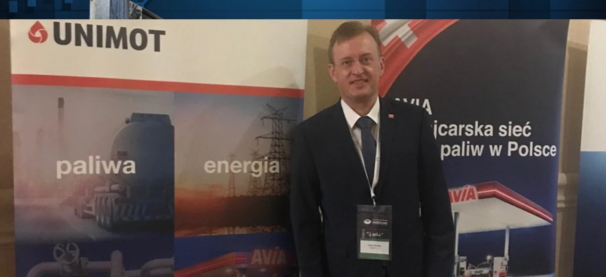 Pracownik umysłowy w garniturze i marynarce stoi obok banerów reklamowych. Słowa kluczowe: Praca, biznesmen, logo, UNIMOT, Wall St.