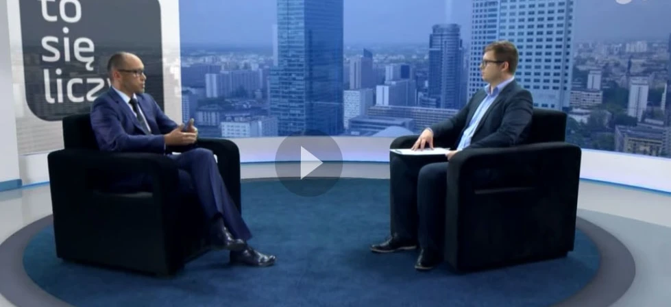 Pracownik umysłowy wygodnie siedzi na stylowym meblu w garniturze i marynarce, czytając wiadomości. Tekst w języku polskim w tle.