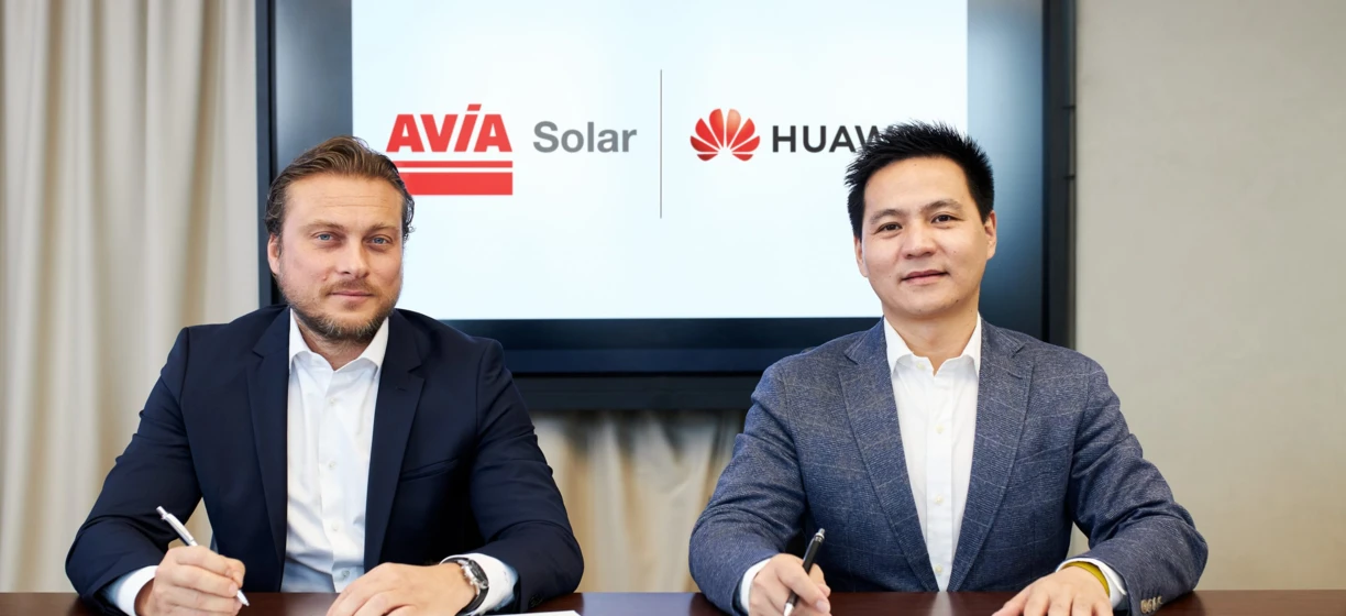 Biznesmen w garniturze współpracujący z kolegami podczas spotkania w firmie. Loga AVÍA Solar HUAV i Huawei widoczne w tle.