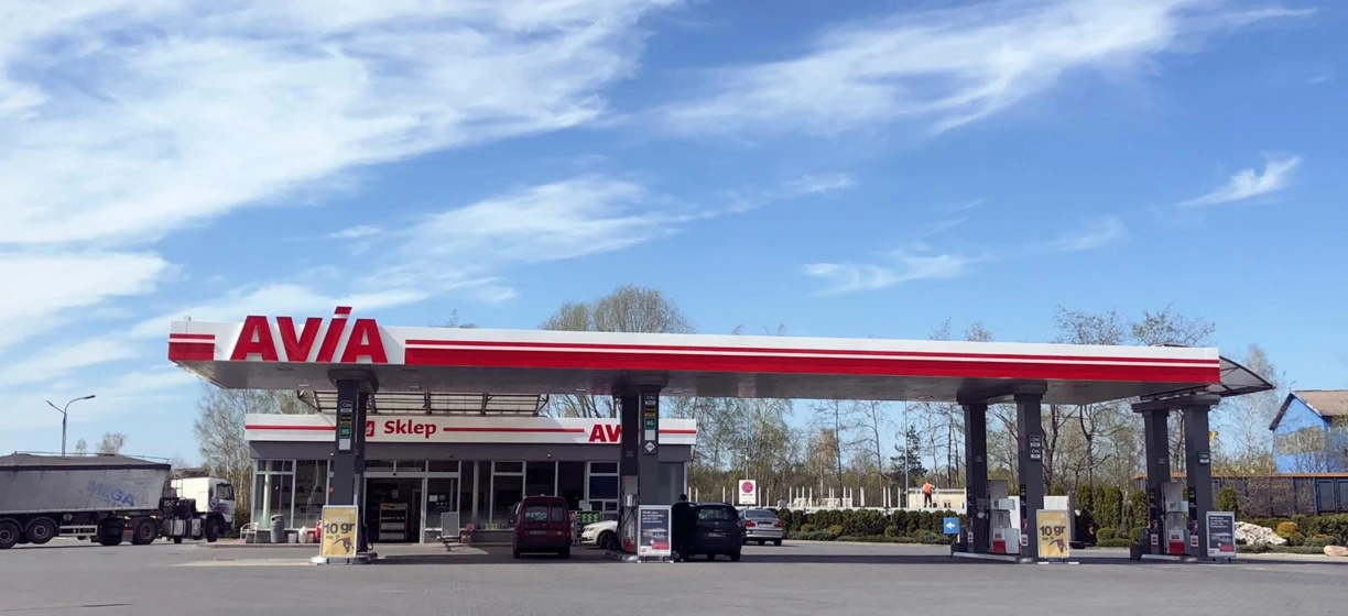 Samochód rodzinny zaparkowany na stacji paliw z widokiem na lustro boczne i zderzak samochodowy. Słowa kluczowe: AVIA, Sklep, MEGA, paliwo, parking samochodowy.