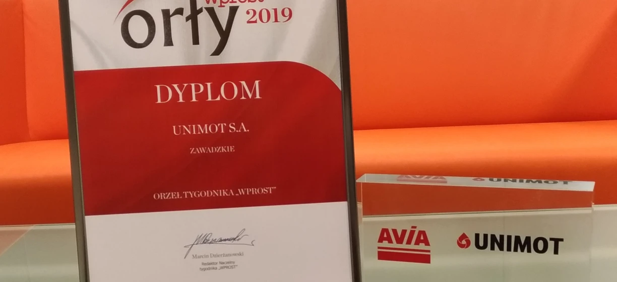 Zdjęcie przedstawiające pomarańczową etykietę z tekstem w różnych czcionkach, w tym logo czasopisma wprost. Przyznane Marcinowi Dzierzanowskiemu z UNIMOT S.A. za rok 2019.