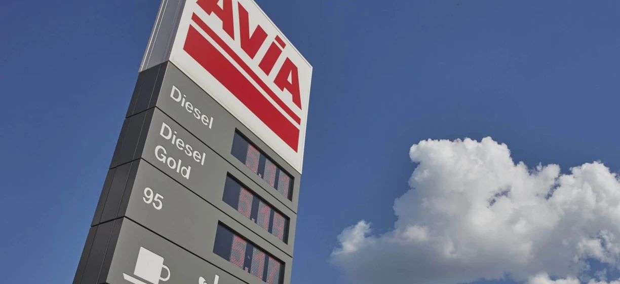 Zblizenie na zloty zapas paliwa AVIA z opcjami na diesel i 95. Odbijajace lustro boczne samochodu na stacji benzynowej w tle.