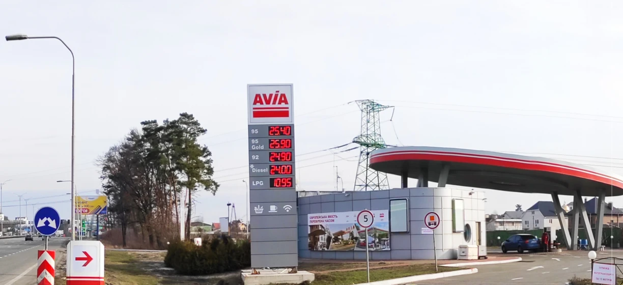 Reklama stacji paliw Avia z cenami benzyny 95 oktanów, Gold, oleju napędowego i LPG. Znak w języku polskim dla Mostu Europejskiego. Samochód miejski zaparkowany przy dystrybutorze paliwa.