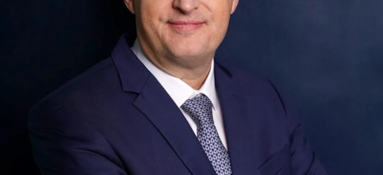 Osoba ubrana w elegancki strój z uczesanymi włosami i poważną miną. Skupienie jest na ich twarzy, kołnierzu i rękawie.