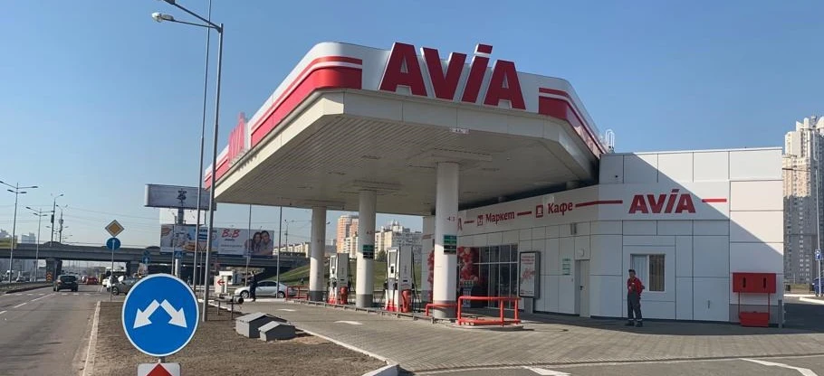 Terenowy pojazd sportowy zaparkowany na stacji benzynowej z pompą AVIA. Lusterka wsteczne odbijają tylne światła i światła stop pojazdu.