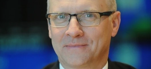 Osoba w okularach z brodą opartą na policzku i kołnierzem widocznym. Zbliżenie na okulary na twarzy.