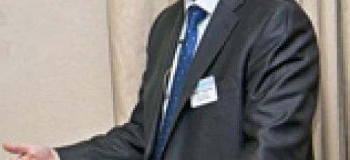 Osoba ubrana w czarny garnitur i okulary, stojąca z ręką na ramieniu. Oficjalny strój i okulary dla dopracowanego stylu.