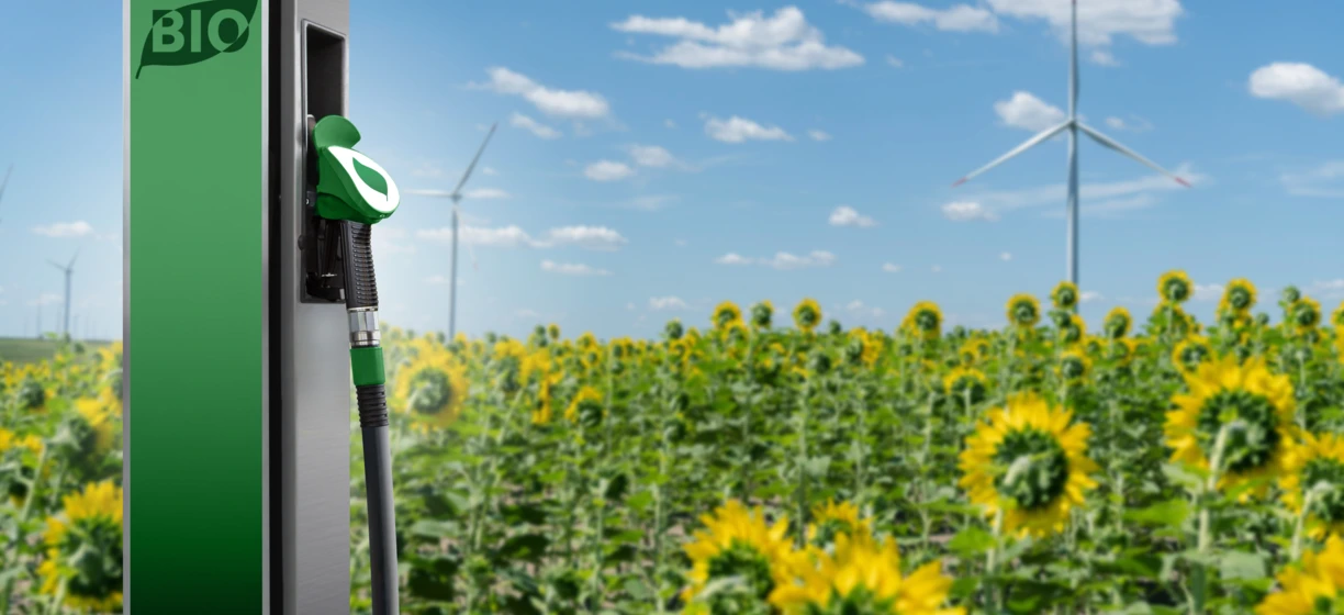 Dystrybutor biopaliwa na tle pola słoneczników i turbin wiatrowych, symbolizujący odnawialne źródła energii i zrównoważony rozwój