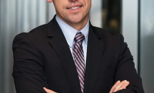 Mężczyzna w eleganckim ubraniu uśmiecha się, nosząc okulary z kołnierzykiem i z podwiniętymi rękawami. Zadbana higiena wzroku jest ważna dla eleganckiego wyglądu.