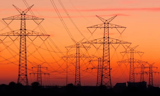 Linia przesyłowa i wieża przesyłowa o zmierzchu, dostarczająca elektryczność do pomarańczowego blasku miasta. Istotna część sieci elektroenergetycznej.