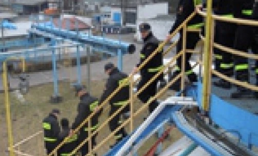 Grupa robotników noszących odzież roboczą o wysokiej widoczności i kaski stoi przy płocie. Załoga jest gotowa na dzień pracy.