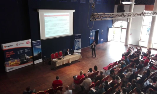 Publiczność na wydarzeniu technologicznym w sali konferencyjnej sponsorowanej przez UNIMOT. Meble, krzesła i urządzenia do wyświetlania elektronicznego są przygotowane na to wydarzenie.