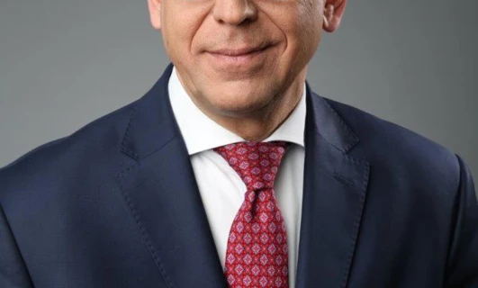 Osoba nosząca okulary, z podbródkiem oprzytym o dłoń, wyróżniająca pielęgnację wzroku i modę okularową. Szczegóły na ramionach, kołnierzu i rękawach są widoczne.