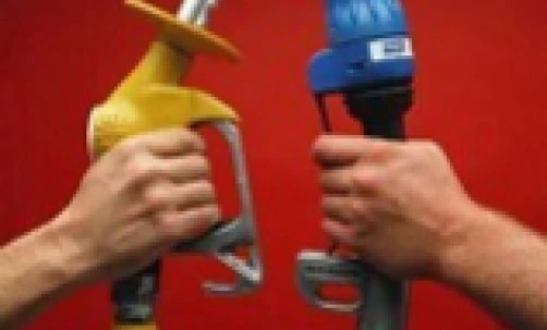 Handlowiec w roboczym ubraniu używa dyszy dystrybutora paliwa, aby napełnić maszynę paliwem przez rurę i wąż.