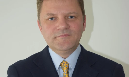 Zbliżenie obrazka mężczyzny w czarnym żakiecie i krawacie, pokazującego jego podbródek, brew, czoło i kołnierzyk, gdy pewnie pozuje.