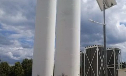 W przemyśle inżynier sprawdza cylindryczny materiał kompozytowy. W tle widoczne maszyny i rury.