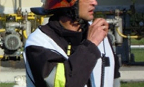 Robotnik fizyczny noszący osobistą odzież ochronną, w tym kask i odzież odblaskową. Na obrazku widzimy pracownika służb ratowniczych, być może strażaka, w swoim ubraniu roboczym.