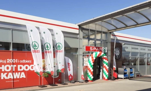 Logo AVIA na stacji benzynowej z reklamą hot dogów, kawy i pizzy. Lokal do wynajęcia z podanym numerem telefonu.