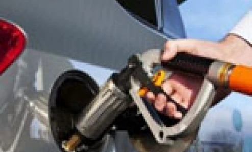 Dystrybutor paliwa na stacji benzynowej obok samochodu z otwartymi drzwiami i czyszczonym przednim szybą. Opieka nad pojazdem z napędem elektrycznym i maska w tle.