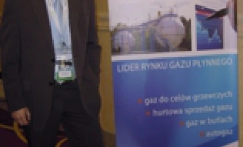 Pracownik biurowy w eleganckim żakiecie i spodniach garniturowych z koszulą i krawatem, reklamujący UNIMOT Gas jako lidera na rynku. Wyraźnie widoczne logo FLF.