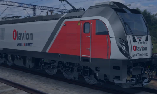 Elektryczna lokomotywa poruszająca się po torze, z wycieraczkami na przedniej szybie i włączonym reflektorem. Skupienie na ESACTadb-000.