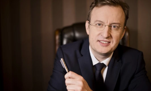 Zbliżenie osoby noszącej okulary i garnitur z palcem spoczywającym na brodzie. Opieka nad wzrokiem i formalne ubranie są tutaj podkreślone.