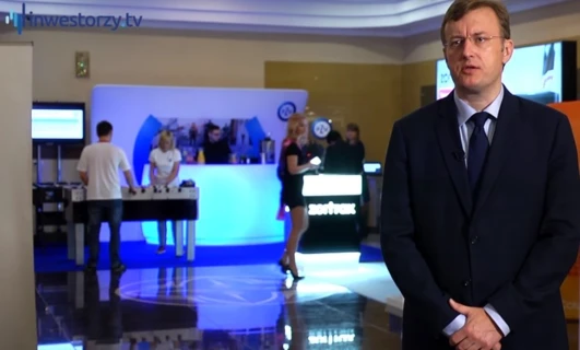 Pracownik biurowy w białym garniturze korzystający z urządzenia wyświetlającego do transmisji multimedialnych, prezentujący technologię inwestorom w telewizji.