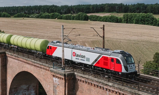 Lokomotywa elektryczna na torach kolejowych z innym taborami. Maszyna transportu publicznego firmy GRUPA & UNIMOT. Model Olavion S1 51 3 180 482-4 PL-CL.