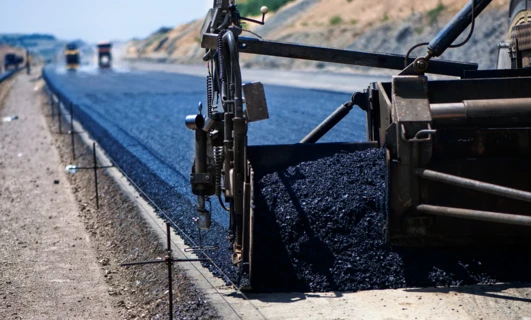 Duża maszyna układająca świeżą asfalt na nawierzchni drogi. Zasadniczy sprzęt ciężki do budowy materiałów takich jak beton i żwir na autostradzie.