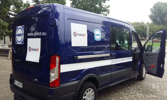 Tekst alternatywny: Widok boczny kompaktowego vana z logo PIMOT i Tankuj24. Elementy obejmują lusterko boczne, zderzak, drzwi samochodu i kołpak. Pojazd użytkowy Ford Motor Company.