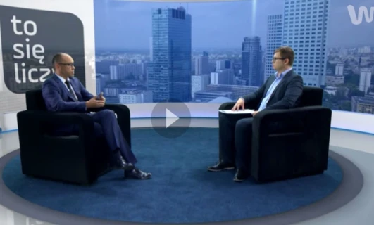 Pracownik umysłowy wygodnie siedzi na stylowym meblu w garniturze i marynarce, czytając wiadomości. Tekst w języku polskim w tle.