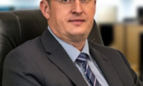 Biznesmen w eleganckim ubraniu siedzący w okularach i koszuli, symbolizujący profesjonalizm i troskę o wzrok.