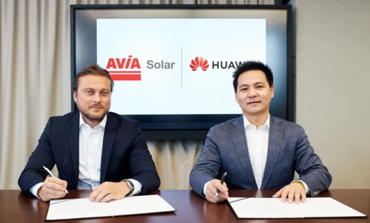 Biznesmen w garniturze współpracujący z kolegami podczas spotkania w firmie. Loga AVÍA Solar HUAV i Huawei widoczne w tle.
